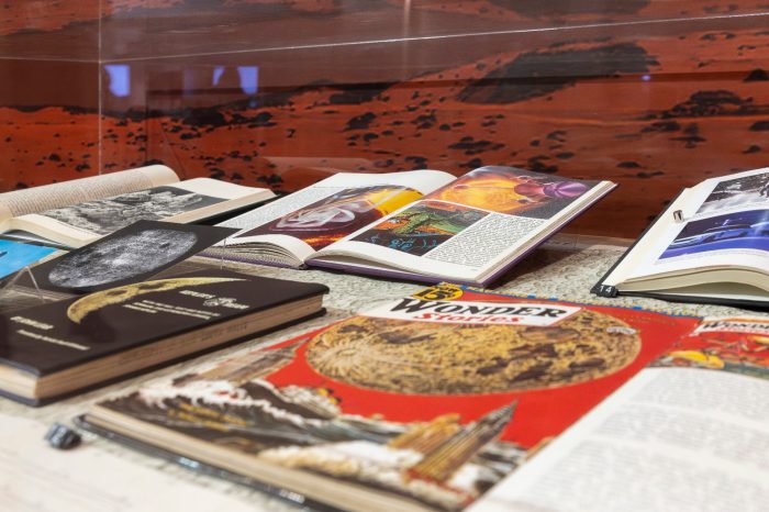 A display case filled with open science fiction books and vintage magazines, including a retro cover titled "Wonder Stories".