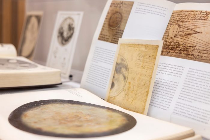 An open book displaying scientific text, historical illustrations of planetary bodies, and images of manuscripts inside an exhibition display case.