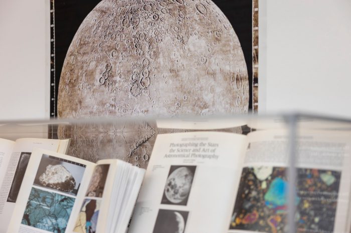 Books displayed in a glass case below a large, detailed poster of the Moon's cratered surface.