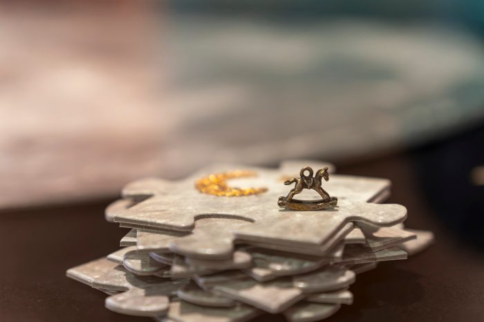 Close-up of stacked moon patterned puzzle pieces in a display case, topped with a small rocking horse charm and a crescent-shaped gold ornament.