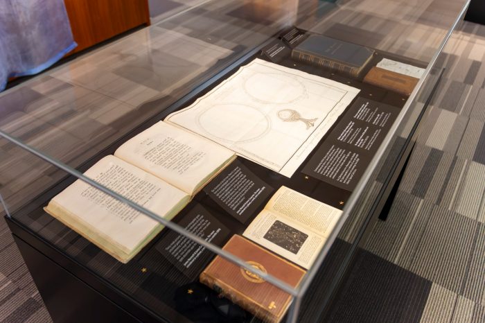 Glass display case containing rare books, open manuscripts, star charts, and astronomy-related publications, with exhibition labels.