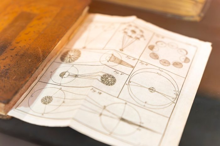 Close-up of an open historic astronomy book displaying detailed celestial diagrams and orbital illustrations, presented inside a display case.