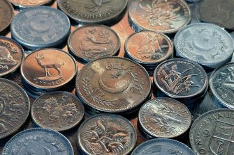 A close-up, high-angle photo of mixed international coins on a reflective surface. The image includes coins from Pakistan, the United States, Canada, and various other nations, highlighting their different metal textures, dates, and engravings.