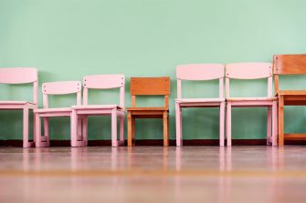 A row of pink and orange wooden school chairs in various sizes.
