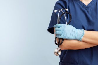 Close up of a health professional in blue scrubs and gloves holding a stethoscope.