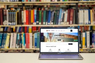A laptop with UNSWorks homepage on its screen. The laptop is on a desk in front of a row of Library bookshelves.