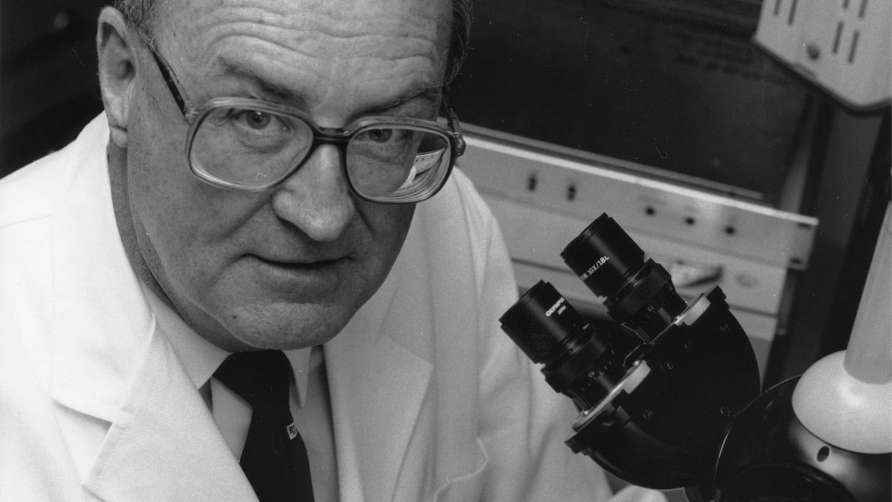 Black and white photo of a professor in a lab coat with a microscope