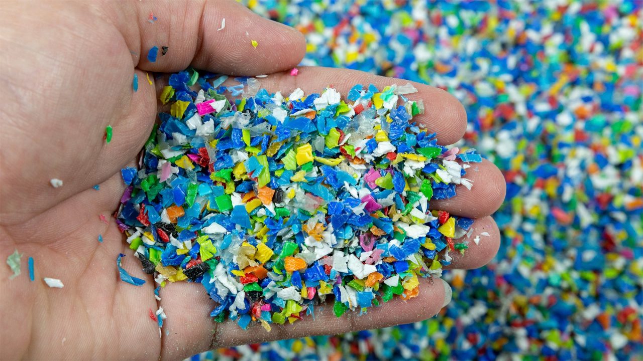 Close up of a hand scooping up a handful of colourful plastic pieces.