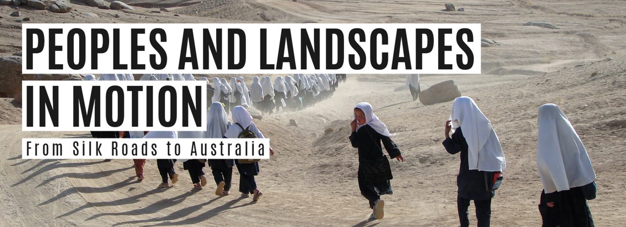 A group of children dressed in long flowing fabric run away from the camera in a desert landscape