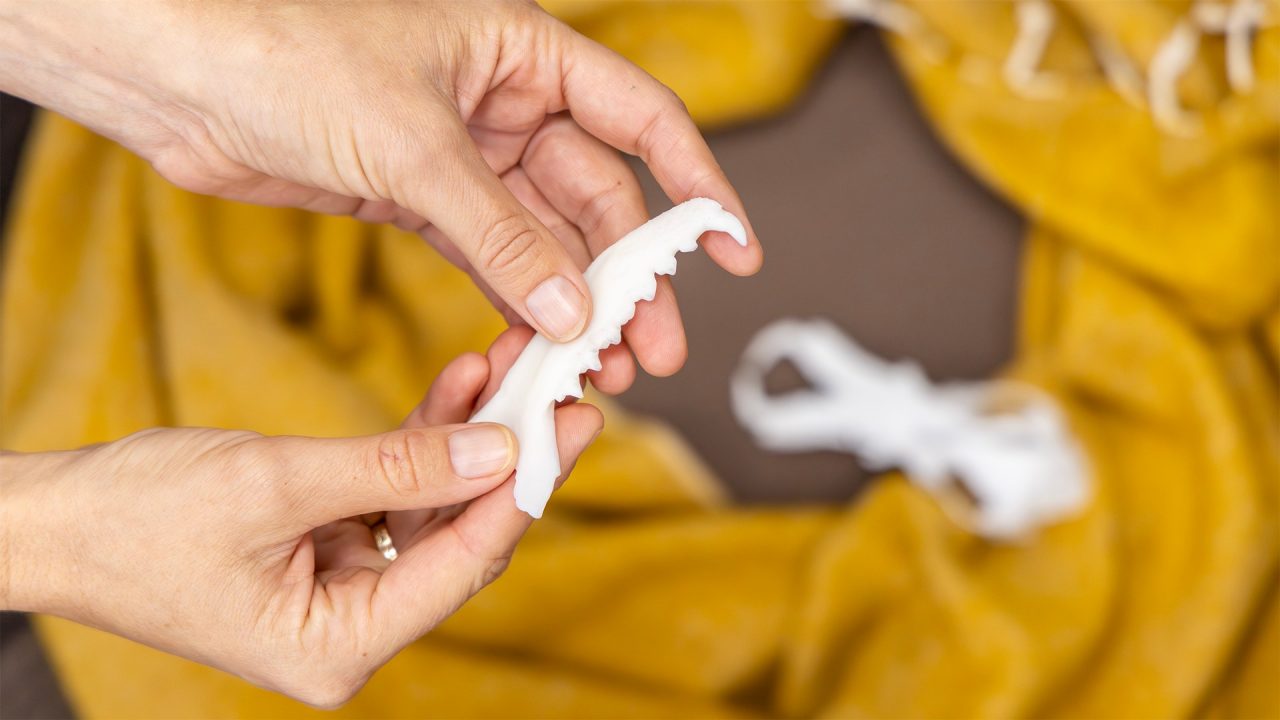 Close up of a pair of hands holding a white fossil bone, on a backdrop of mustard yellow coloured cloth.