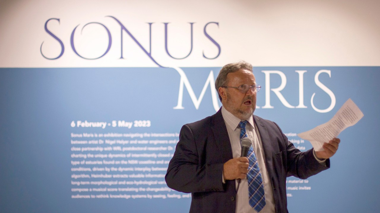 A man in a suit giving a speech in front of a blue and white wall.