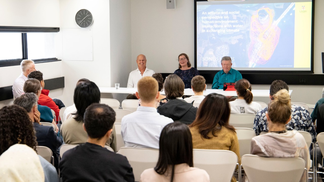 A panel of three people face an audience in a seminar room
