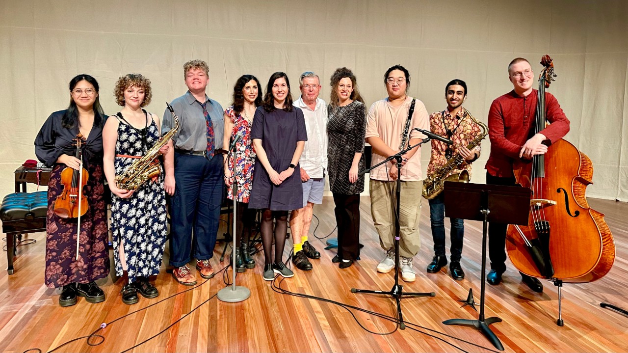 Several people with musical instruments stand on a stage facing the camera smiling