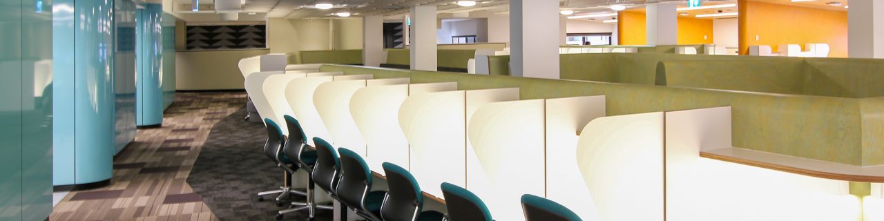 A row of invidiual study desks each with a light and dividers between them.